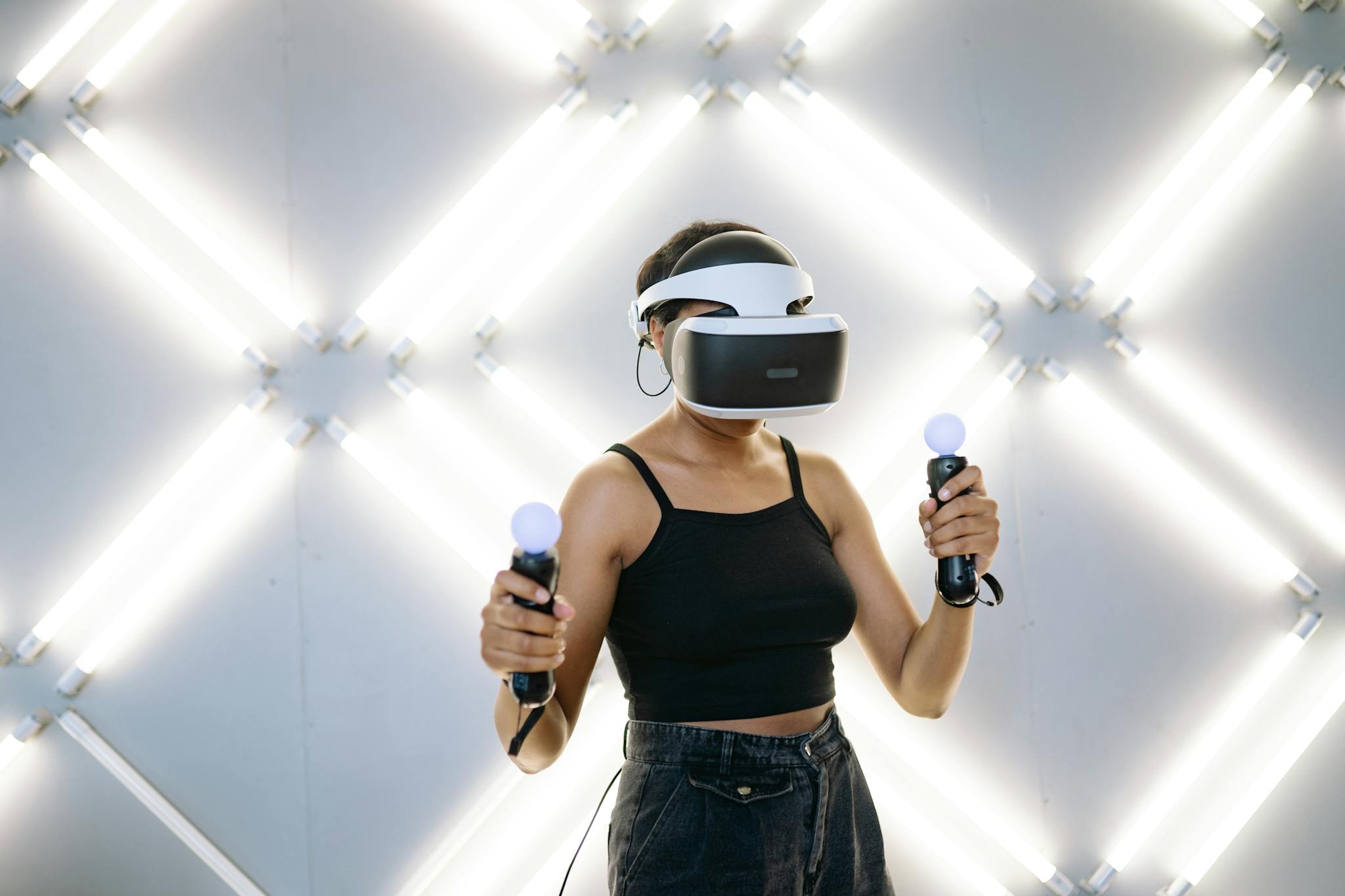 Young woman in a studio playing virtual reality games with VR headset and controllers.